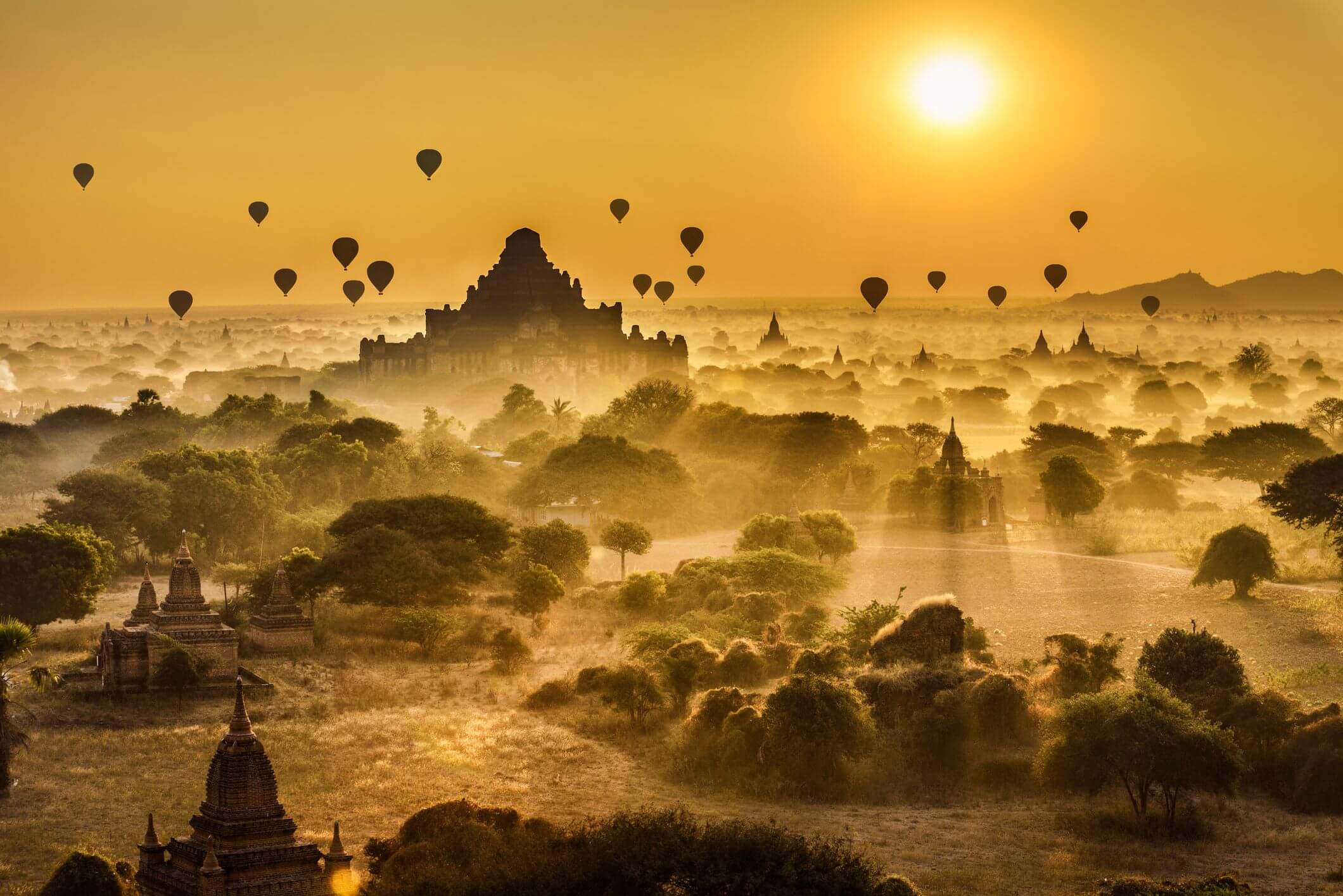 Scenic view of ancient temples in misty landscape with hot air balloons
